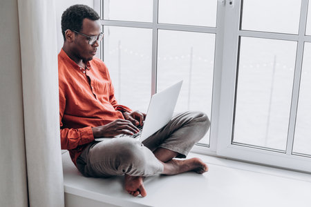 African American Man Working on Laptop at Home with a Sea Viewの写真素材