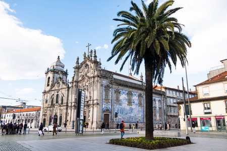 A stunning church adorned with traditional blue azulejo tiles stands in Porto, with a vibrant palm tree in the foreground of a lively square.のeditorial素材
