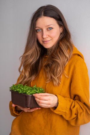 A contented woman in a mustard blouse holds a brown pot of dense microgreens, a nod to healthy eating and urban farming practicesの写真素材