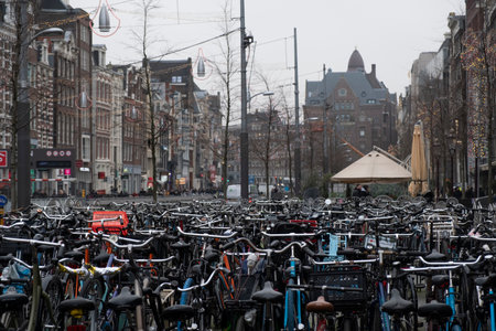 A dense sea of parked bicycles dominates the foreground with Amsterdams classic architecture and city life blurred in the background.のeditorial素材
