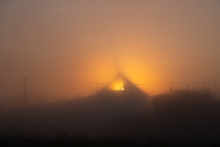 House Silhouette in Foggy Sunrise with Orange Glowの写真素材