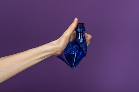 Woman Hand Holding Crushed Blue Plastic Bottle Against Purple Background