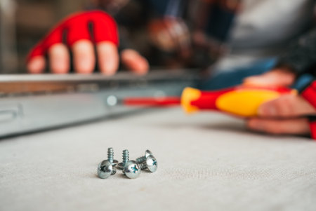 Close-up of screws and screwdriver, with person wearing red gloves working on DIY project in...