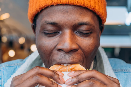 Close-up of African American man savoring bite of burger, capturing moment of enjoyment and taste.