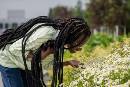 Happy woman with dreadlocks enjoys aroma of daisies in parkの写真素材