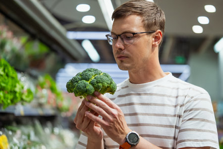 Man Selecting Fresh Broccoli in Supermarket Produce Sectionの写真素材