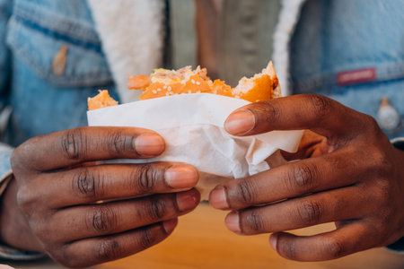 Close-up of black man Hands Holding a Half-Eaten Burger Wrapped in Paper