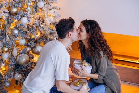 Couple Kissing by Decorated Christmas Tree with Presents. Man and woman exchanged Christmas gifts in cozy atmosphere.の写真素材
