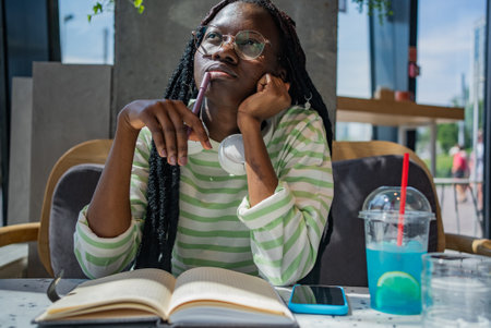 Young Black Woman Thinking and Writing in Cafe with Blue Drink lemonadeの写真素材