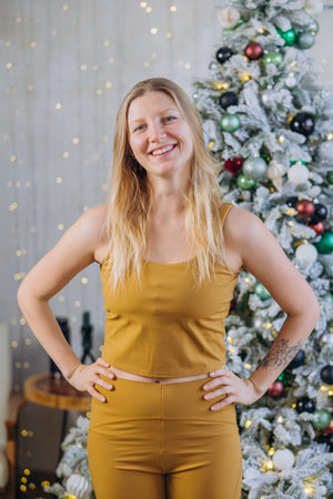 Smiling Woman in Gold Outfit Posing in Front of Decorated Christmas Treeの写真素材