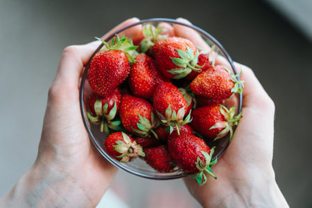 Woman Hands holding a bowl of fresh red strawberriesの写真素材