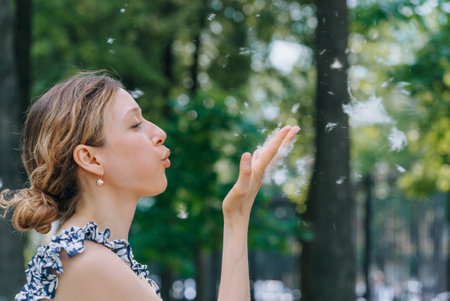 Woman blowing poplar fluff in park on sunny day. The flowering of the poplar, the time of seasonal allergies.の写真素材