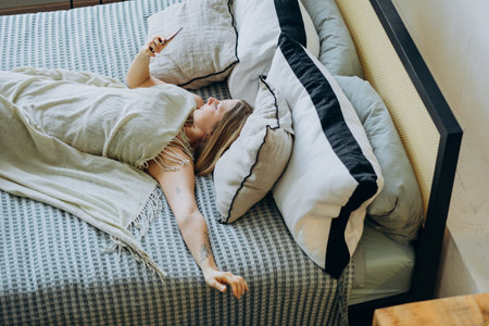 Woman Relaxing in Bed with Phone and Cozy Blanketの写真素材