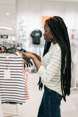 African American Woman with dreadlocks selects for striped shirts in clothing store