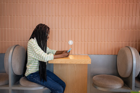 Black woman with dreadlocks sitting in cafe using smartphone at wooden tableの写真素材