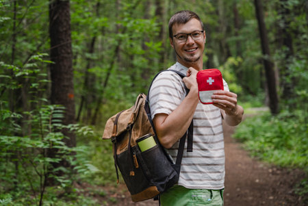 Smiling hiker man with backpack holding first aid kit in forest