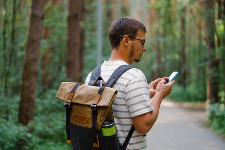 Man Hiking in Forest with Backpack, Checking Smartphone for Navigation or Messagesの写真素材