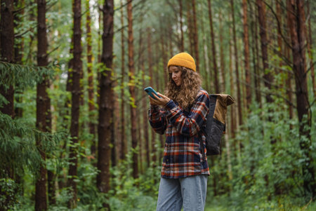 Woman Hiking in Forest with Backpack, Using Smartphone for Navigation, Outdoor Adventureの写真素材