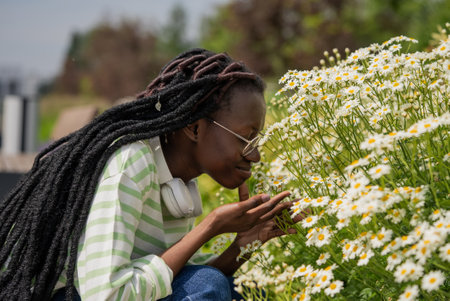 African woman enjoying the scent of chamomile in summer city gardenの写真素材