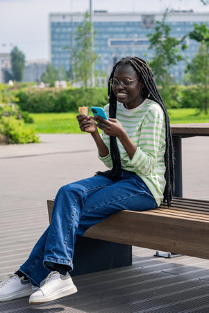 Smiling woman watching funny content on internet on smartphone and eating ice cream outdoorsの写真素材