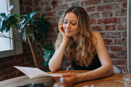 Woman reading menu in cozy cafe, sitting at wooden table with brick wall backgroundの写真素材