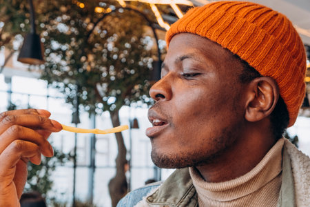 African American man eating french fries in food court of shopping mall in fast food cafeの写真素材