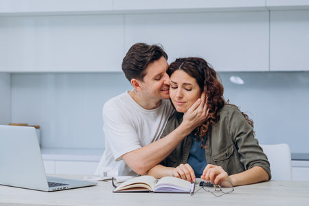 Man comforts woman while working at home on laptop, kisses on cheek and hugsの写真素材