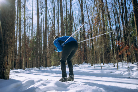 Man cross-country skiing through snowy forest, rear view of skier during outdoor winter workout
