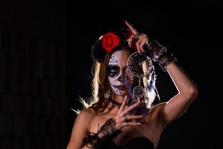 Woman in Day of the Dead makeup holding dreamcatcher in dark settingの写真素材