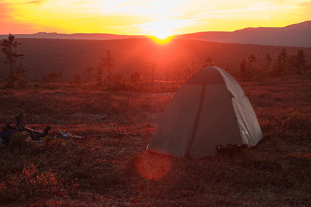 Camping tent and hiking backpack lying in grass at sunset in wildernessの写真素材