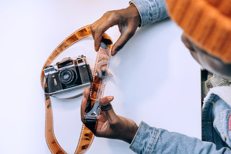 Black African American man looking at negatives on 35mm photographic film with vintage camera on tableの写真素材