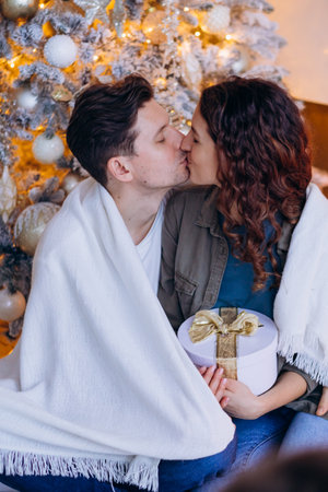 Couple sharing a kiss by Christmas tree with giftの写真素材