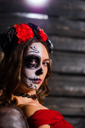 Young woman with sugar skull makeup and flower crown poses in a studio, embodying a festive and artistic vibe for dia de los muertosの写真素材