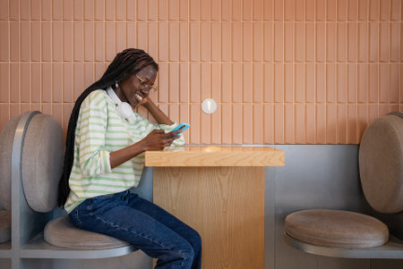 Carefree digital lifestyle: young woman smiling and using smartphone with wireless earphones in a cozy cafeの写真素材