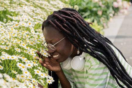 Young woman with dreadlocks happily smelling chamomile flowers in a sunny city park, radiating joy and positivity in a moment of pure serenityの写真素材