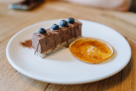 Savor a luscious chocolate cake with blueberries and orange on a white plate in a charming cafe. Luxuriously rich, creamy, sweet, and tangy, ideal for a tasty treatの写真素材