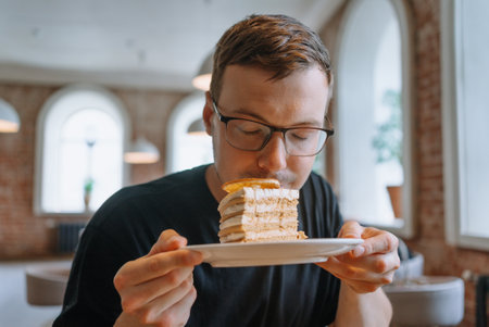Young man savors the aroma of a delectable piece of cake before indulging in the first biteの写真素材