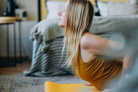Young woman gracefully stretches on a yellow yoga mat in her cozy bedroom, embodying a healthy lifestyle through daily yogaの写真素材