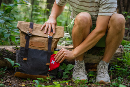 Hiker man placing first aid kit into backpack while resting in a forest