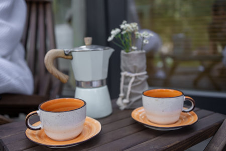Elegant Outdoor Coffee Break: Moka Pot and Ceramic Cups on Wooden Tableの写真素材