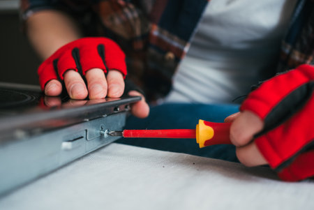 Focused technician wearing gloves tightens screw with screwdriver while working on household applianceの写真素材