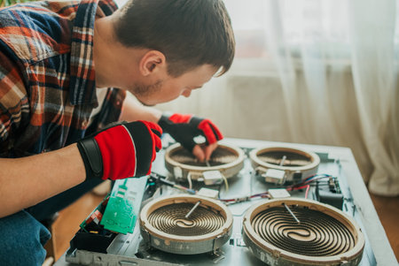 Electrician with gloves carefully repairs modern induction cooker components using a screwdriver in a home settingの写真素材