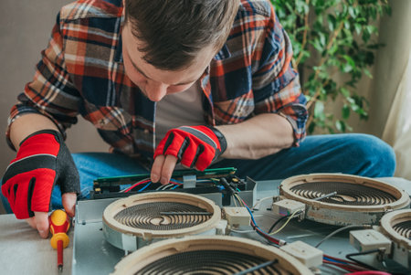 Electrician uses screwdriver to repair burner element on electric stove top, prioritizing safety and efficiencyの写真素材