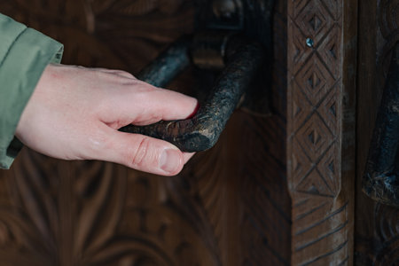 A mans hand is holding onto an antique metal door handle in an antique doorの写真素材