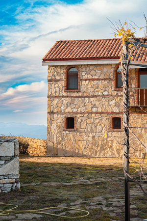 A rustic stone house bathed in the soft glow of dusk stands proudly against a backdrop of distant mountains and a clear sky.の写真素材