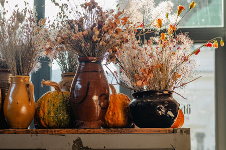 Dried flowers in earthenware pots with pumpkins. Rustic autumnal display on a wooden shelf.の写真素材