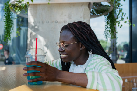 Young woman enjoying a refreshing blue drink at an outdoor cafeの写真素材