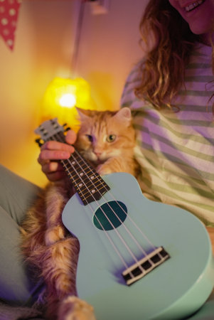 Woman playing ukulele with ginger cat on lap