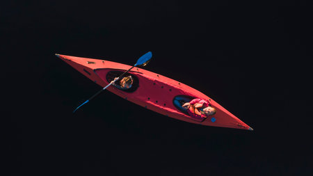 Two women kayaking on dark water in red kayakの写真素材