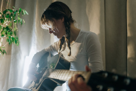 Young woman playing acoustic guitar at homeの写真素材